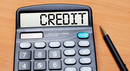 On a wooden table there is a black pen and a calculator with the text CREDIT. Business concept