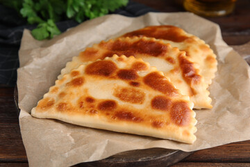 Board with delicious fried chebureki on wooden table, closeup