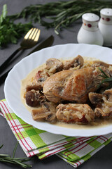 Rabbit meat with mushrooms and sour cream sauce in a white plate on a dark gray background. Vertical format