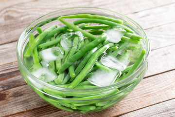 Green beans in a colander. Boiled or blanched vegetables in ice water on a table