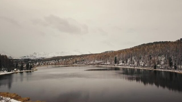 Altai, Siberia, Russia. A lonely wild empty mountain lake in winter with white snow-capped mountains on the background. Snow-covered forests, a highway, reflections in the water. Freedom, loneliness