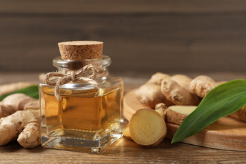 Glass bottle of essential oil and ginger root on wooden table