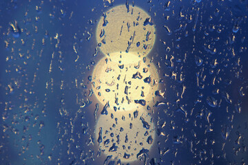 raindrops on the glass of the window against the background of round lights at home in the evening in autumn 