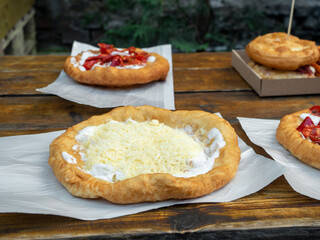 Langos with sour cream and grated cheese on wooden table. Langos - deep-fried flatbread,...