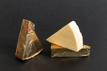 Triangular cream cheeses wrapped in foil and without packaging on a black background. Portioned...