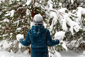 Back view of child boy in winter forest in snowstorm. Kid holding snowball. Actively spending time outdoors. Winter snowy woodland. Cold frost weather in snowstorm. Happy childhood