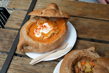 Hungarian goulash in bread bowl on wooden table. Street food in Budapest,  Hungary. - obrazy, fototapety, plakaty