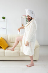 Funny portrait of handsome beautiful guy in towel and bathrobe holding tube of body cream lotion in hand. Spa, body and skin care for man concept