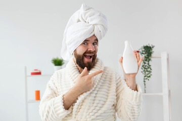 Beauty portrait of handsome beautiful guy in towel and bathrobe holding tube of body cream lotion in hand. Spa, body and skin care for man concept