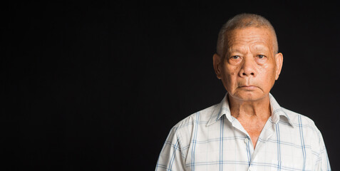 Portrait of an elderly Asian man in a white shirt looking at the camera while standing on black...
