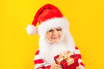 Funny child toddler in a Santa hat with red gift , yellow background. Holidays, Traditions, Christmas concept.