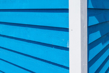 The exterior corner of a wooden building with blue cape cod clapboard siding and white trim board....