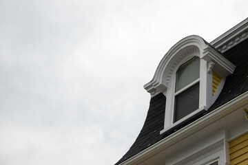 The roof of a vintage green wooden building with cream color trim, multiple double hung windows, dormers, and a green shingled hip roof. It's an old wooden house with multiple stories.
