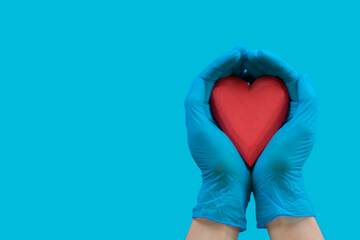 Obraz premium Female hands wearing blue medical latex gloves holding red heart over light blue background. Health care, heart disease, donation, insurance. Top view