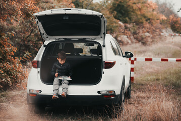 A child is sitting in the trunk of a car SUV or crossover with gouache paints, a car in the autumn forest