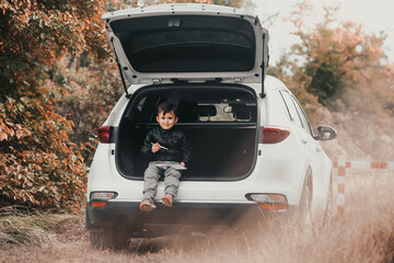 Fototapeta na wymiar A child is sitting in the trunk of a car SUV or crossover with gouache paints, a car in the autumn forest
