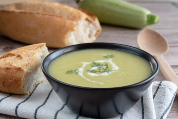 Vegetable squash puree soup. A whole zucchini, slices of bread and a wooden spoon on a wooden background.