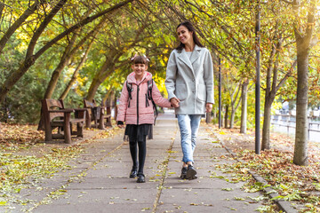 Happy mom and daughter walk in autumn park. Little girl after school with mother. Everyday life