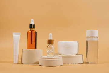 Copy space geometric shapes made of concrete with day cream serum, cosmetic oil, eye cream on beige background. Unbranded bottles in mockup style. Beauty background with facial cosmetic products.