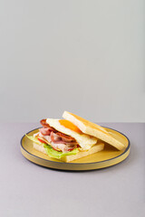 Breakfast sandwich with egg, bacon and vegetables on grey close-up
