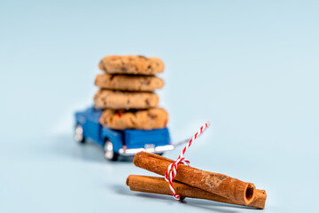 A toy car carries cookies with chocolate and cinnamon sticks on a blue background. Holiday card for New Year and Christmas