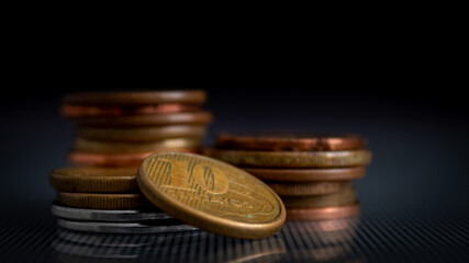 moedas empilhadas em superfície de vidro, refletindo no vidro, em um fundo escuro, com o foco em uma moeda de 10 centavos de BRL. 