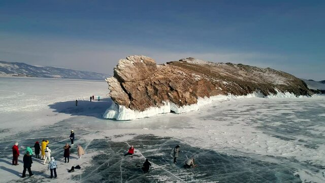 Aerial view on the rocky ice covered island in lake Baikal. Groups of tourist walking around on the cracked ice. Famous tourist spot. Beautiful winter landscape of lake Baikal