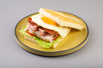 Breakfast sandwich with egg, bacon and vegetables on grey close-up