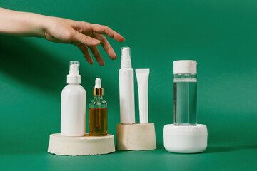 Unbranded bottle with dispenser on geometric podium. Woman's hand touches day cream cosmetic oil, eye cream on green background. Unbranded bottles in mockup style. Beauty, natural cosmetics concept.
