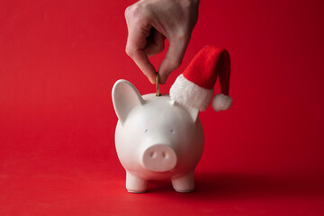 Hand putting money into a piggy bank wearing a santa hat. Christmas savings background