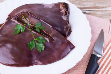 Raw liver on a white plate on a wooden background. Beef liver, top view. Offal in its raw form.