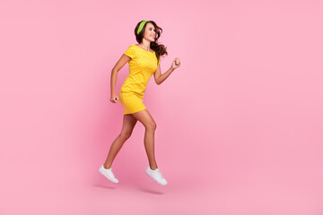 Fototapeta na wymiar Photo of hurrying fast young woman wear yellow dress smiling jumping high running looking empty space isolated pink color background