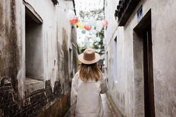 Stylish young caucasian woman 30 years old with blonde hair wearing casual clothing and traveling to China at Autumn. Person outdoor from behind