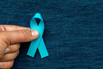 hand holding blue ribbon with bow on blue jeans background. Blue november. Prevention of prostate...