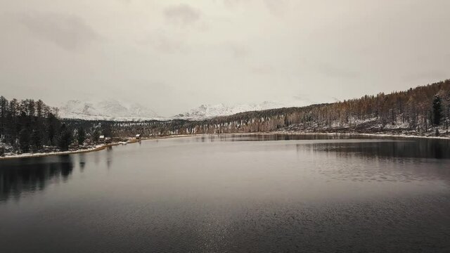 Altai, Siberia, Russia. A lonely wild empty mountain lake in winter with white snow-capped mountains on the background. Snow-covered forests, a highway, reflections in the water. Freedom, loneliness