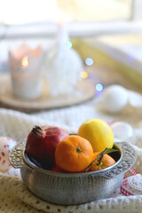 Silver bowl with various fruit, soft blanket and various Christmas decorations. Hygge at home. Selective focus.