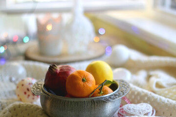 Silver bowl with various fruit, soft blanket and various Christmas decorations. Hygge at home. Selective focus.