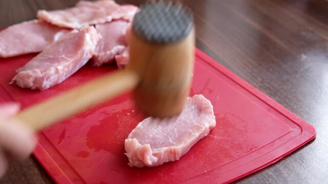 closeup female hands beating raw fresh meat with a wooden mallet, concept of cooking steak chops at home in the kitchen
