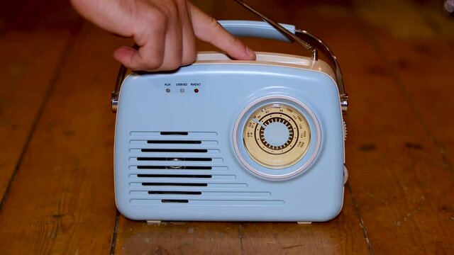An old blue radio with a males mans hand pressing the buttons on the radio