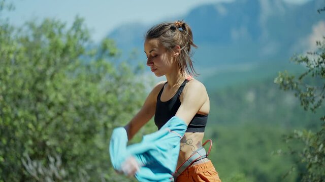 young slim sporty woman rock climber on natural background. girl prepares to climbing and takes off her longsleeve, staying in sport top and showing her strength fitness body and beautiful core