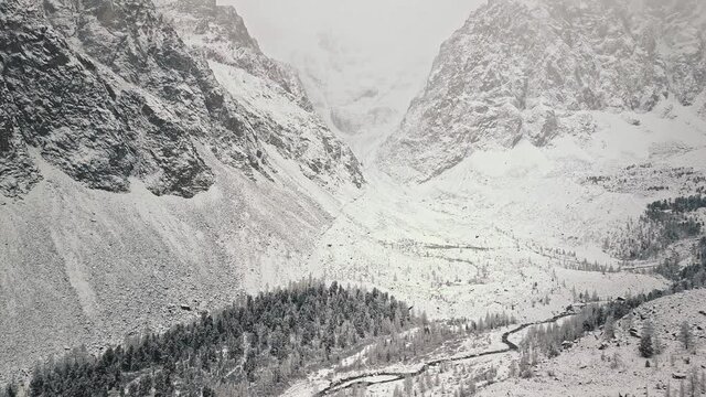 Storm, snowfall in the huge glacier of Mount Belukha, the valley of the Aktru River, the Altai Mountains. Cloudy weather, stone in the snow, storm, wildlife, winter forest, frozen mountain river in