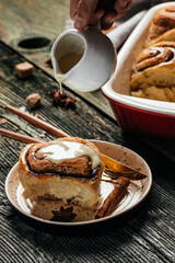Cinnabon. Woman's hand spreading vanilla icing freshly baked cinnamon rolls, vertical image. top view. place for text