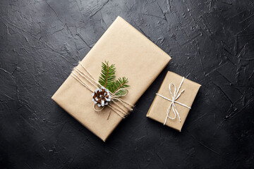 Gift boxes and green Christmas tree branch with cone on dark background top view