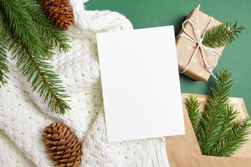 Christmas greeting card mockup with gift box, fir tree branches with cones on knitted background