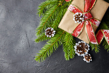 Gift box and green Christmas tree branch with cone on black background top view