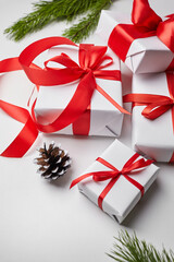 Christmas gift boxes with red ribbon and green pine tree branch with cones on white
