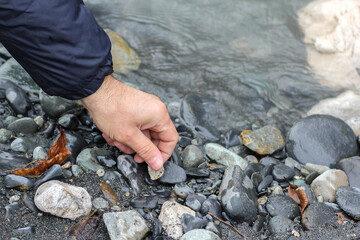 Man hand picking up stones from river beach
