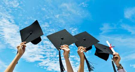 Four hands holding graduation hats on background of blue sky - obrazy, fototapety, plakaty