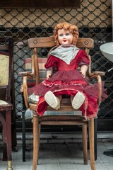 vintage doll in red dress sitting in an old chair outdoors at a flea market