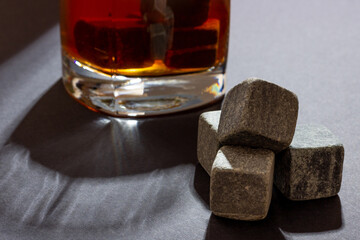 Transparent glass with whiskey on a dark background with bright rays of light. Whiskey stones in a...